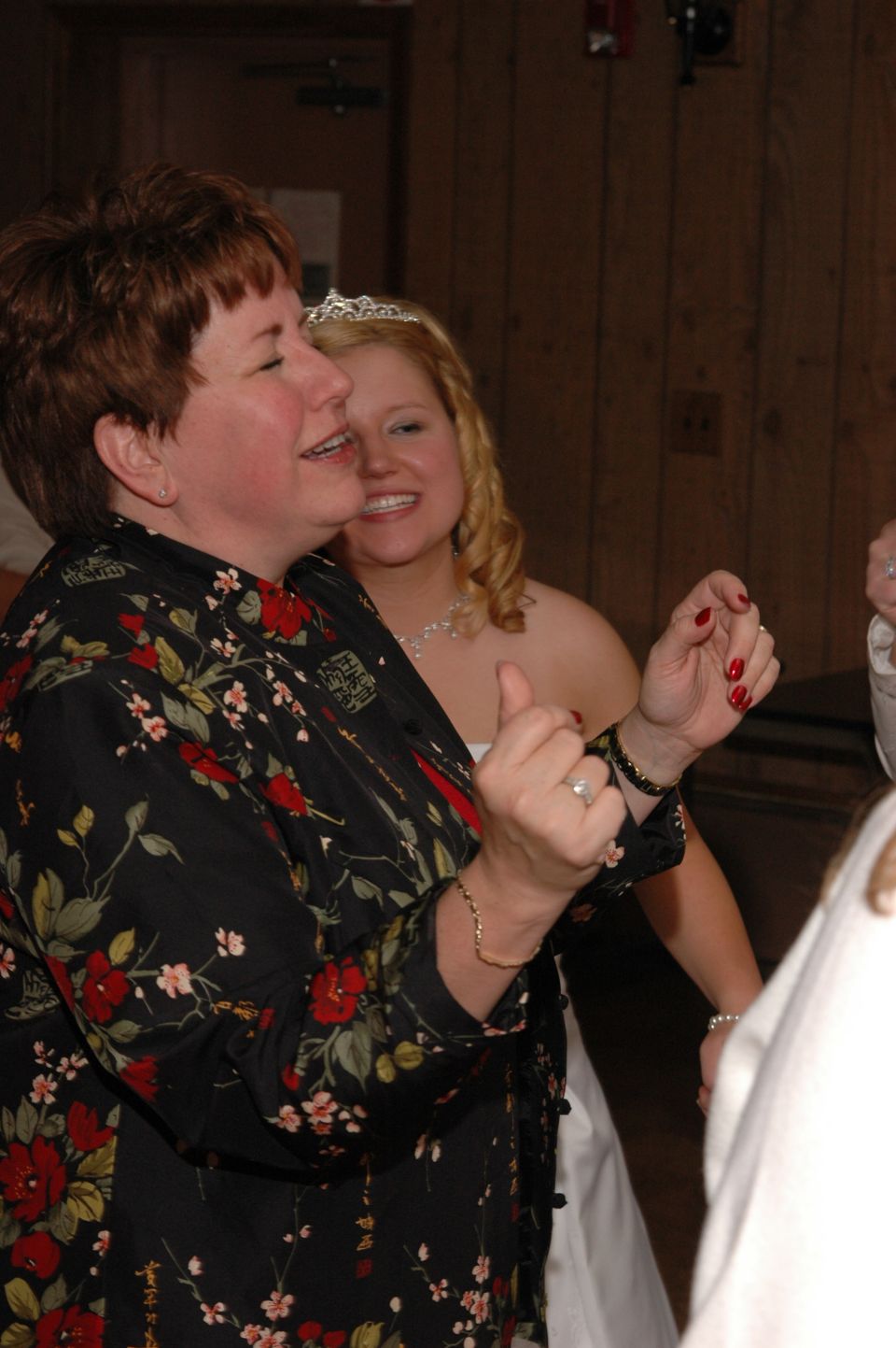 woman in floral shirt dancing, bride in background