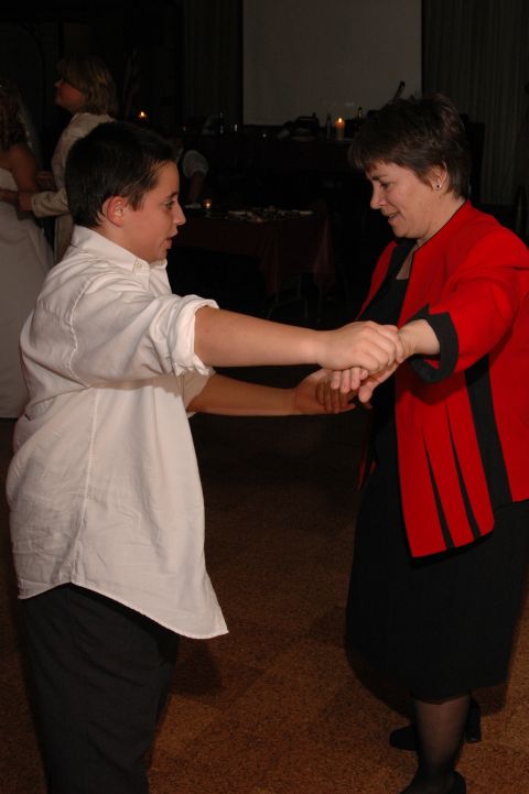 Two people, one in a white shirt and one in a red jacket, holding hands and dancing