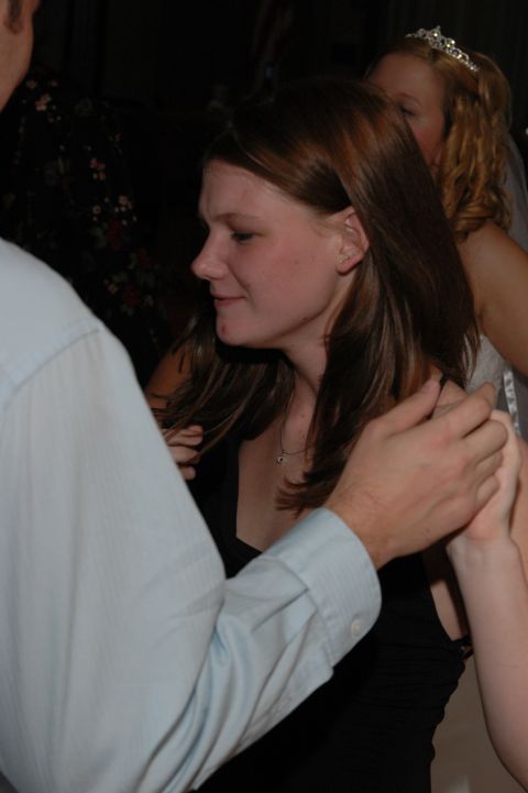 Woman in black dress with hands on her arms, another woman with a tiara behind her