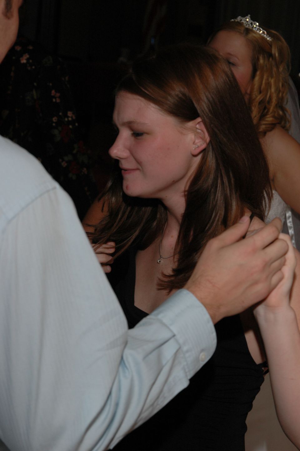Woman in black dress with hands on her arms, another woman with a tiara behind her