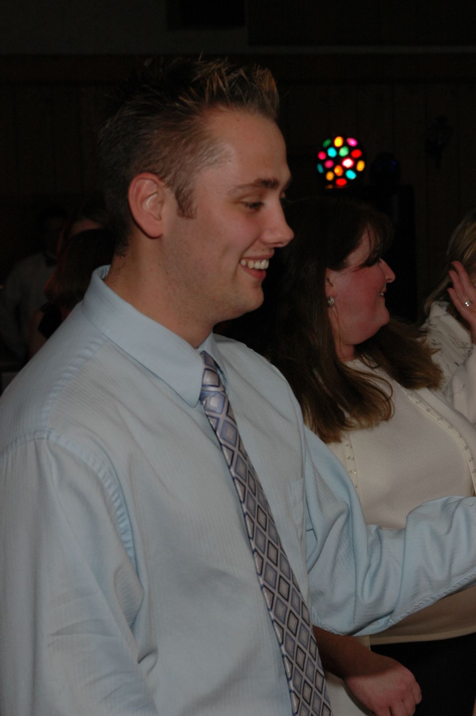 Man in a light blue dress shirt and tie smiles at a party with a disco ball in the background