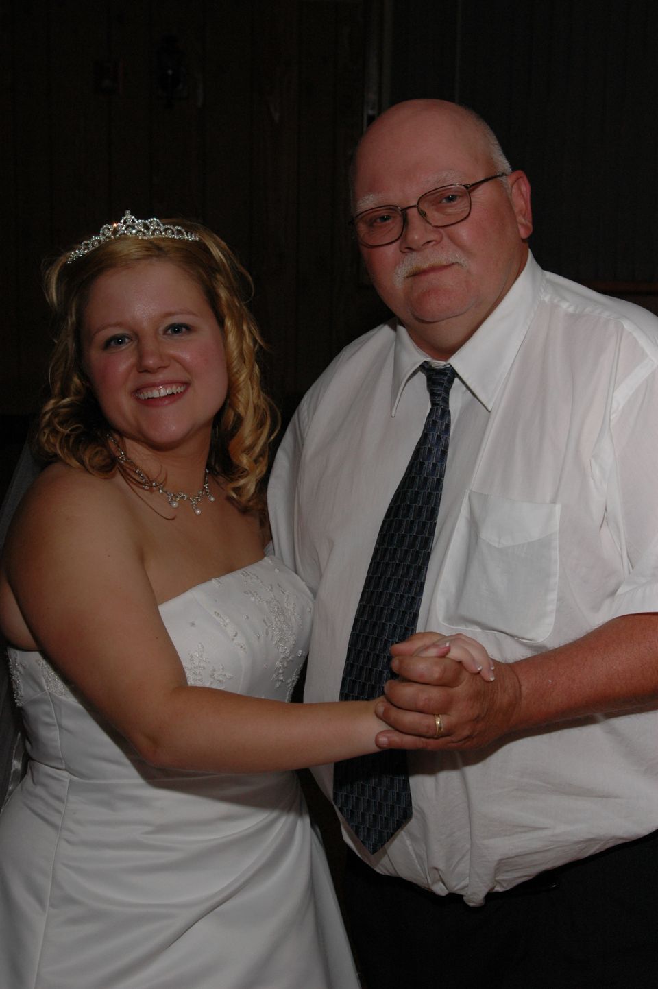 Bride in a white wedding dress and tiara dances with a man in a white shirt and tie