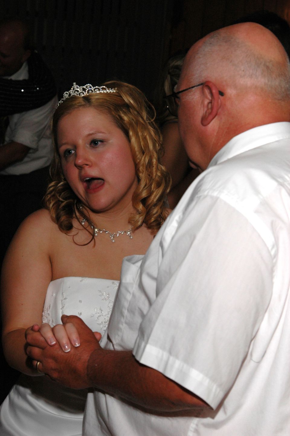 Bride in a white strapless dress and tiara dances with a man in a white shirt