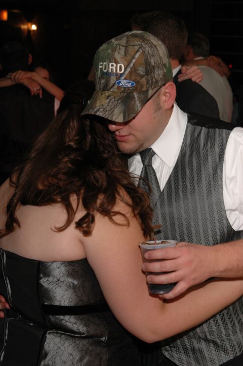guy in a camo Ford hat and vest holding a drink, dancing with a woman