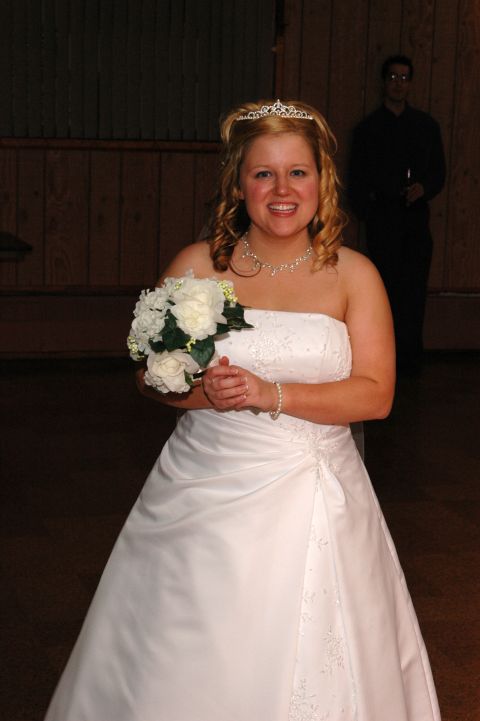 Bride in a white dress holding a bouquet, with a man in the background