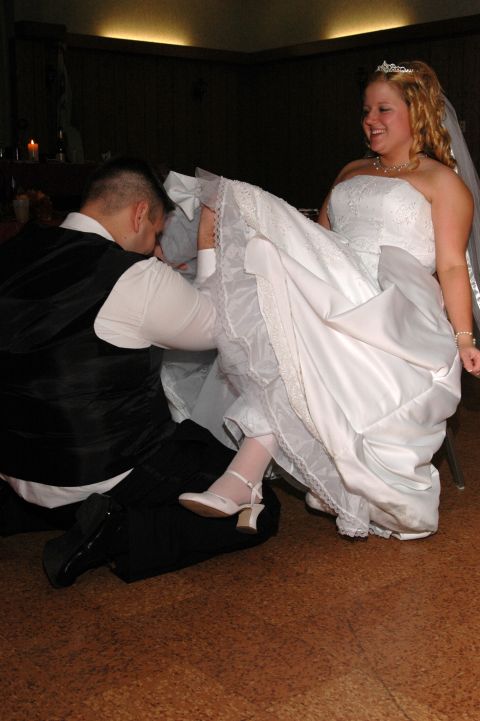 Bride in a white wedding dress and groom in a black vest and white shirt, groom is kneeling and kissing bride'