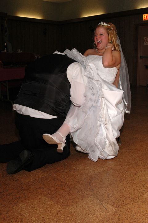 Bride laughing with her leg up, groom kneeling