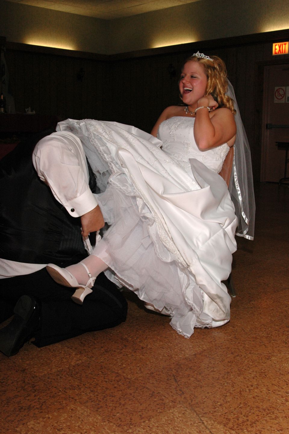Bride in wedding dress laughing, with groom kneeling beside her
