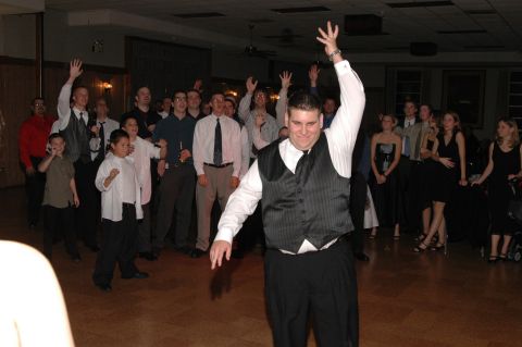 Group of people dancing indoors at a formal event, one man in foreground with arms raised