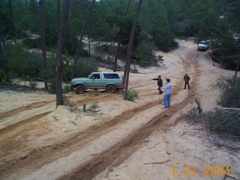 1992 Ford Bronco - A 1992 Ford Bronco navigates a sandy off-road trail with companions observing.