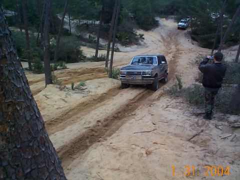 1992 Ford Bronco - A group of vehicles navigates a sandy trail through a wooded area.