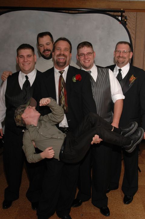 Groom and groomsmen posing for a photo, one groomsman is being held up by another