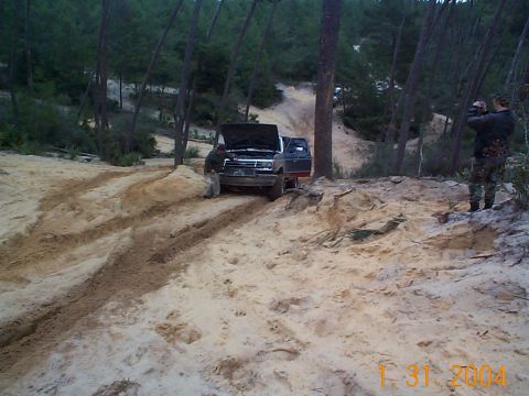 1992 Ford Bronco - A group of people are gathered around a stuck Ford Bronco in a sandy, wooded area.