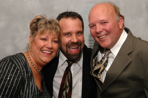 Three smiling people in formal wear against a grey backdrop