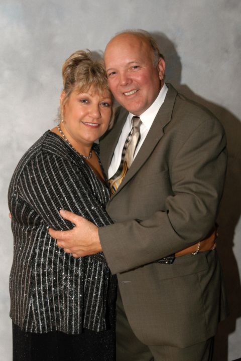 Couple embracing in formal attire against a grey backdrop