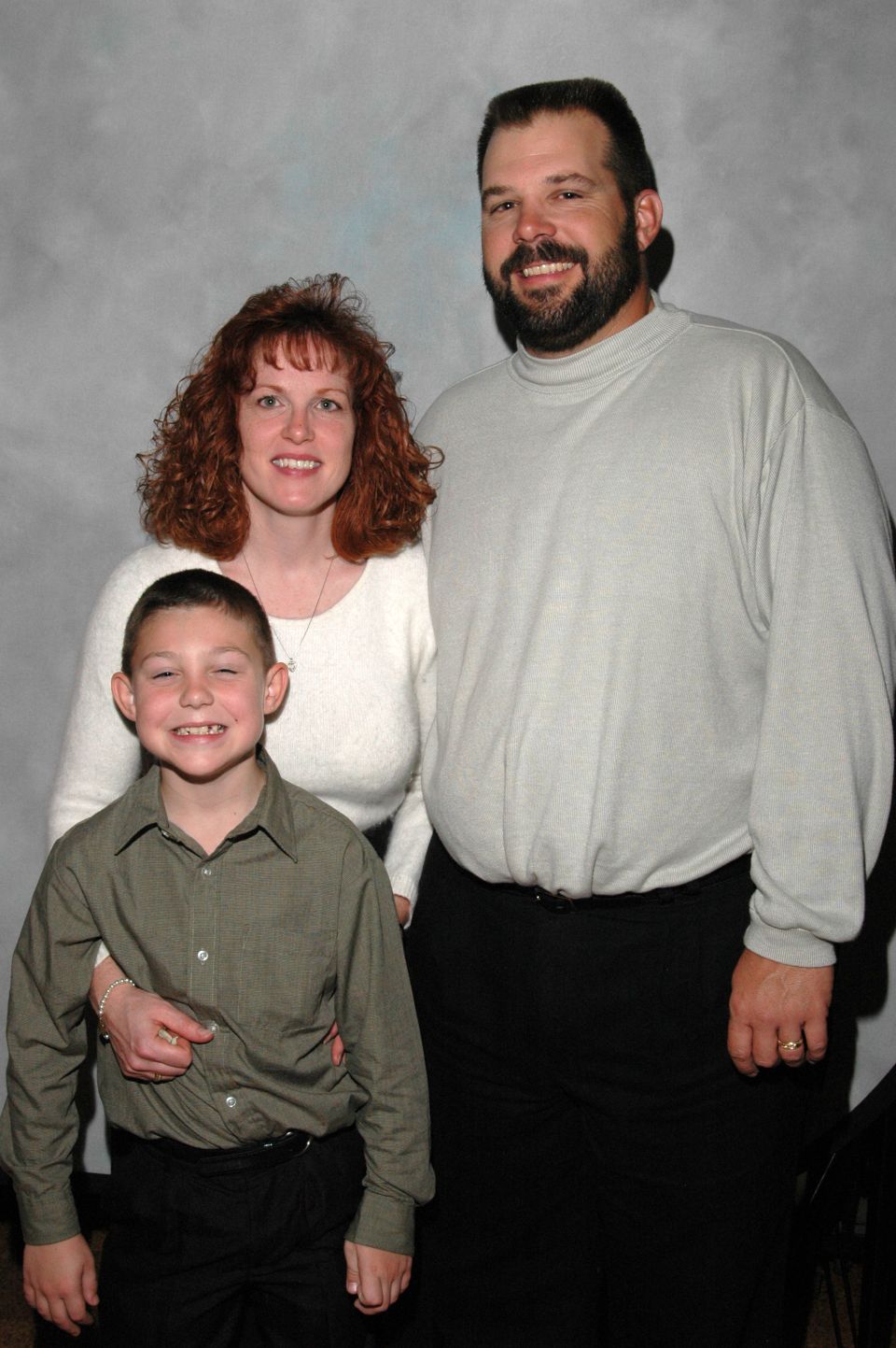 Family of three posing for a portrait against a grey backdrop