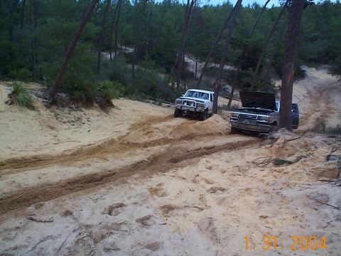 1992 Ford Bronco - Two SUVs navigate a sandy trail through a wooded area, with one vehicle's hood open.