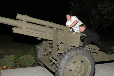 Two boys climbing on a large, olive-drab military howitzer at night