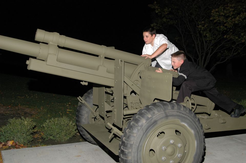 Two boys climbing on a large, olive-drab military howitzer at night