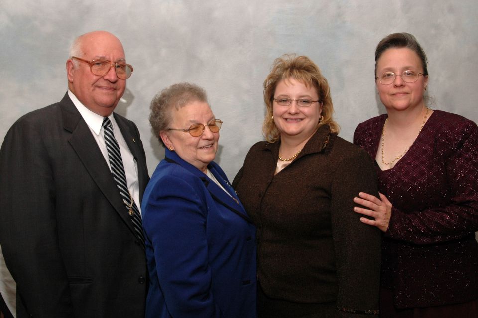 Four people, two men and two women, pose for a formal portrait against a gray backdrop