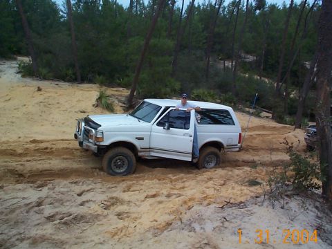 1992 Ford Bronco - A white Ford Bronco navigates sandy terrain, with another vehicle partially visible in the background.