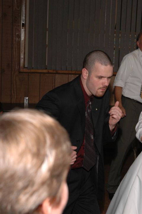Man in a suit and tie dancing at an indoor event with other people visible