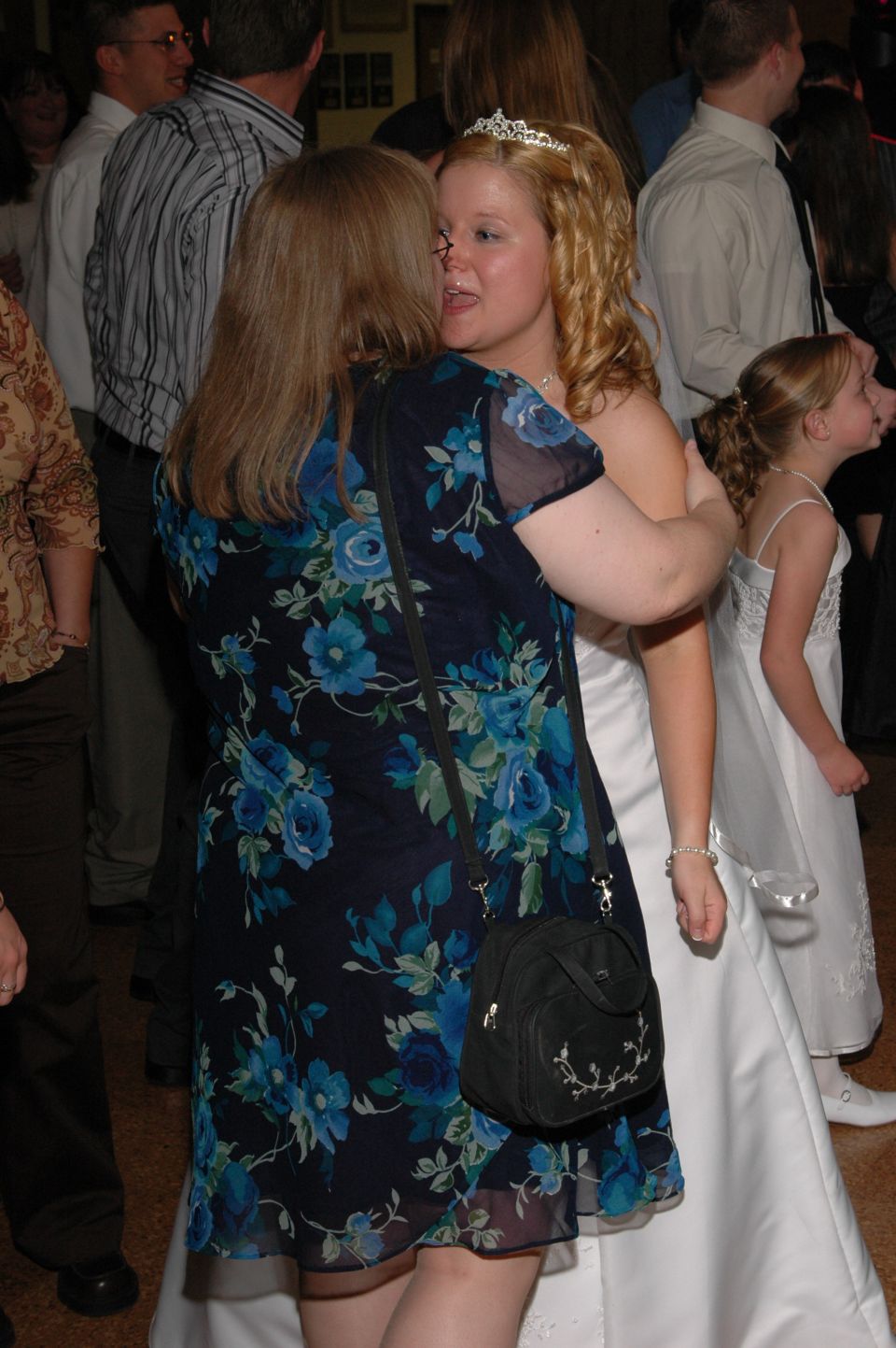 Bride hugging a woman in a floral dress, with a flower girl nearby