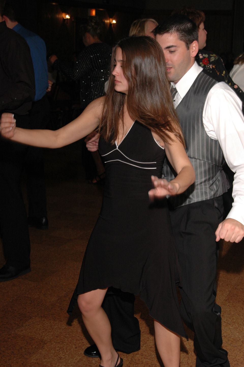 People dancing at an event. A woman in a black dress dances with a man in a vest