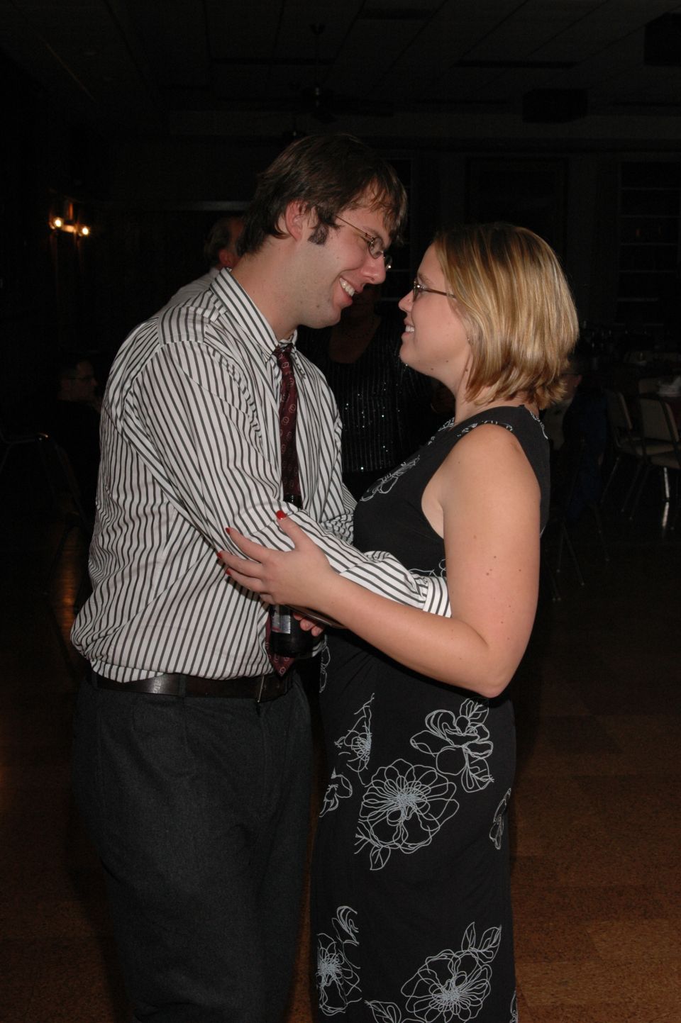 Couple dancing at an event. Man wears a striped shirt and tie, woman wears a floral dress