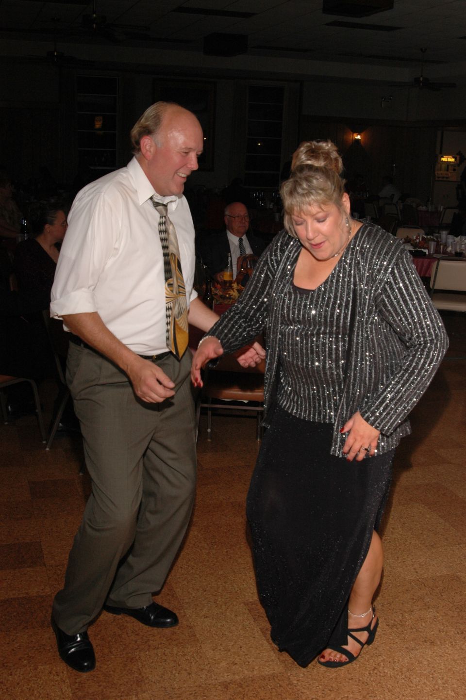 Couple dancing at a formal event. Man in white shirt and tie, woman in sparkly top and black dress