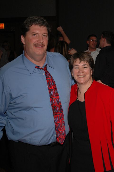 Man in blue shirt and red tie with woman in red jacket at a party