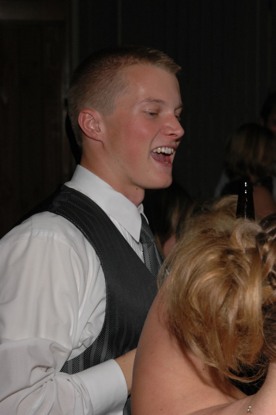 Man in a white shirt and grey vest laughs at a formal event
