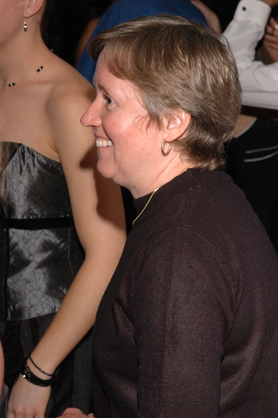 Woman smiling in profile, wearing a dark sweater and hoop earrings