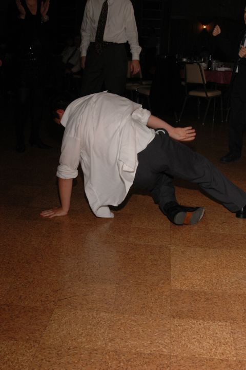 Person in white shirt and dark pants breakdancing on a wood-grain floor