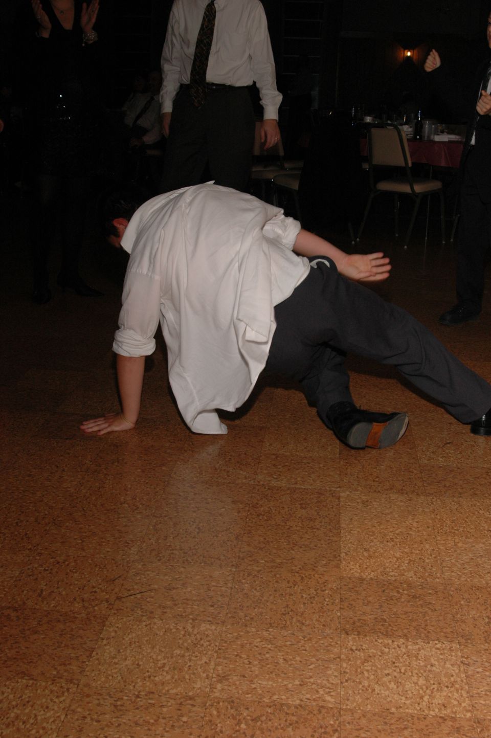 Person in white shirt and dark pants breakdancing on a wood-grain floor