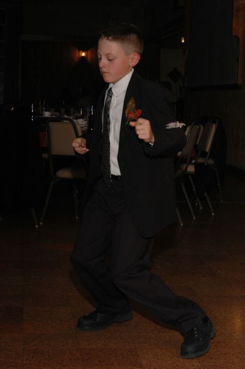 Boy in a black suit and tie dancing at a formal event