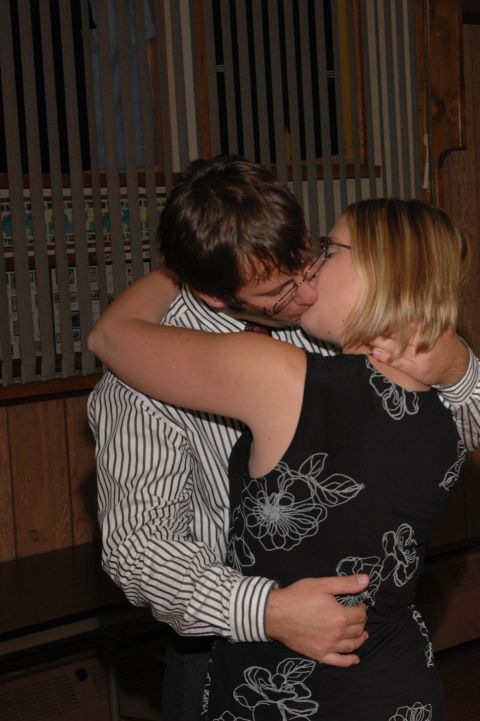 Man and woman kissing indoors. He wears a striped shirt, she wears a floral dress