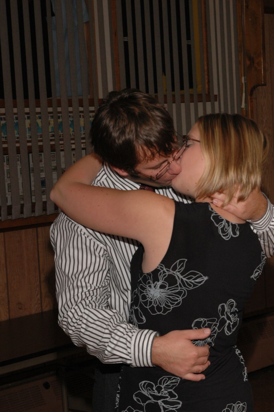 Man and woman kissing indoors. He wears a striped shirt, she wears a floral dress