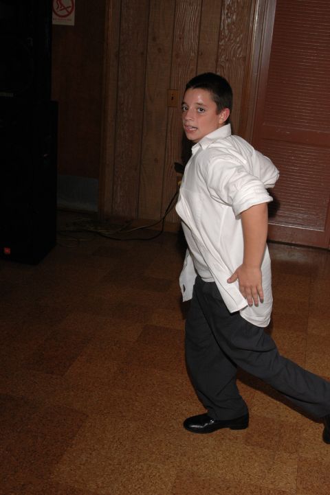 Boy in white shirt and dark pants looking back, standing on wood floor