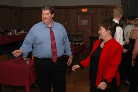 Man in blue shirt and tie dancing with woman in red jacket at indoor event