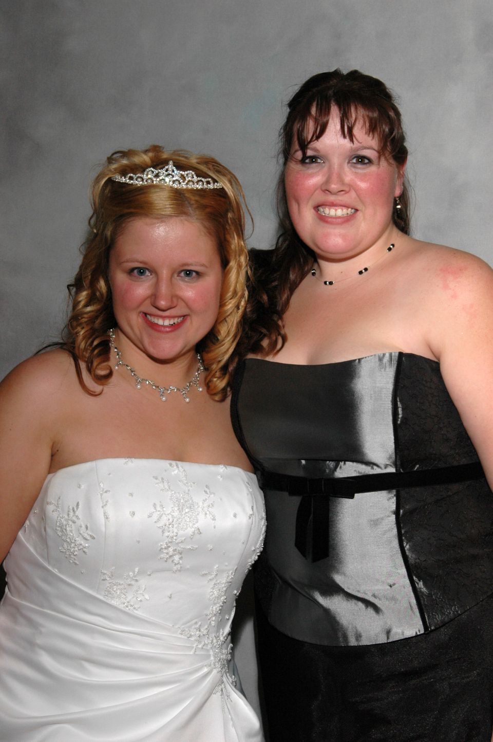 Two women posing for a photo, one in a white wedding dress and tiara, the other in a dark dress