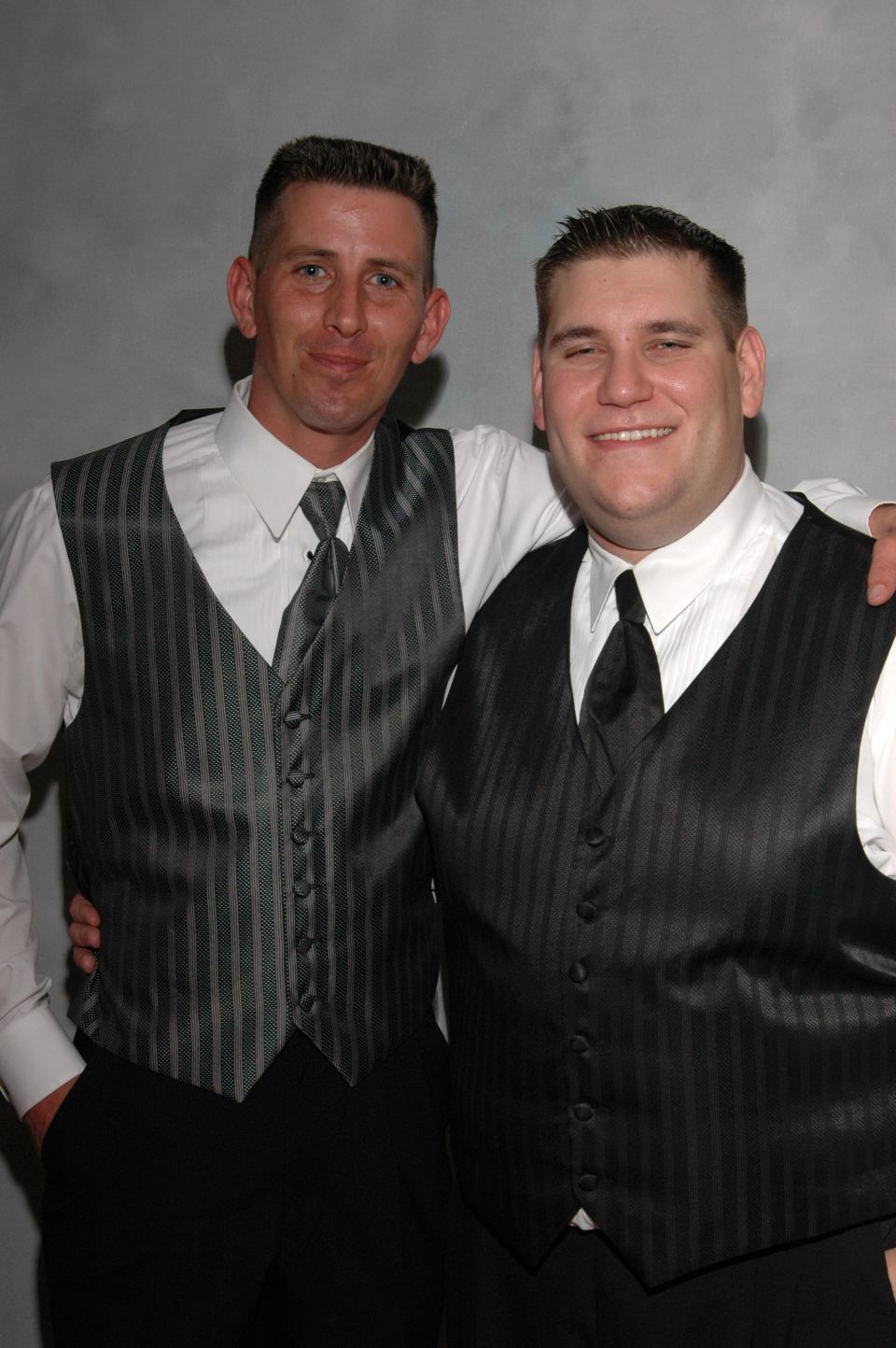 Two men in matching vests and ties stand with arms around each other