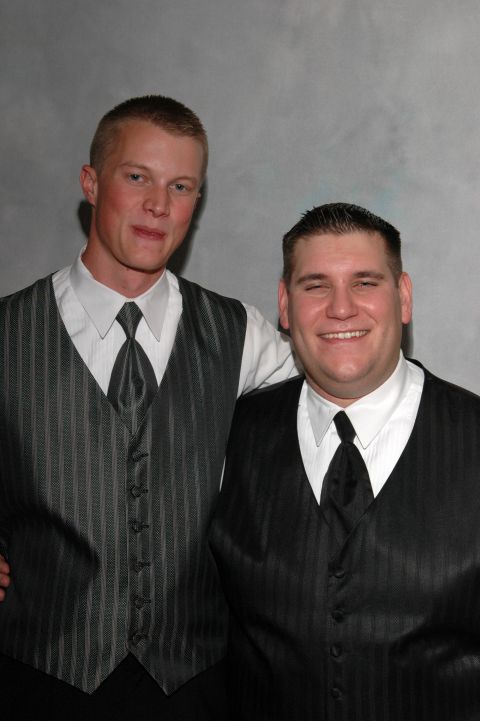 Two men in formal wear, one in a grey pinstripe vest and the other in a black pinstripe vest