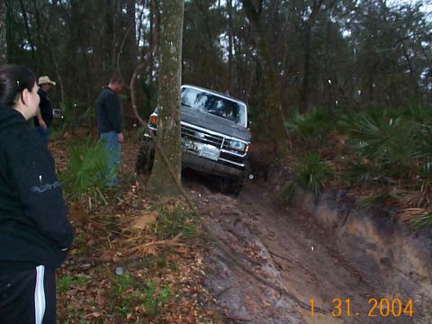 1992 Ford Bronco - A 1992 Ford Bronco tackles a challenging muddy incline in a wooded off-road area.