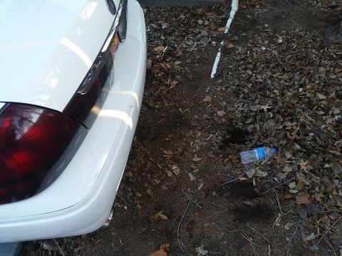 2000 Mercury Grand Marquis - Rear view of a white 2000 Mercury Grand Marquis showing its quarter panel and taillight, with a discarded water bottle on the ground.