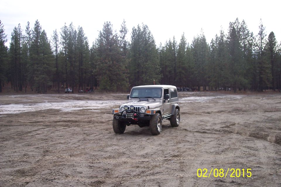 Silver 2-door Jeep Wrangler parked on dirt with trees in background. This is a 2005 Jeep Wrangler