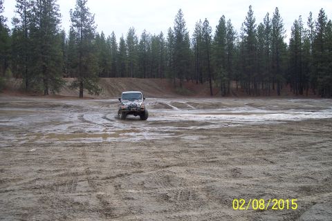 2005 Jeep Wrangler - A silver Jeep Wrangler navigates a wet, muddy terrain surrounded by a dense forest.