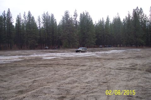 2005 Jeep Wrangler - A Jeep Wrangler navigates a muddy off-road area with a line of trees and other vehicles in the distance.