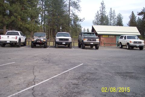 2005 Jeep Wrangler - Several SUVs and trucks are parked in a lot near a building and trees.
