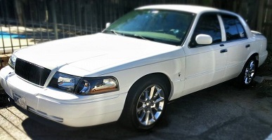 2000 Mercury Grand Marquis - White 2000 Mercury Grand Marquis sedan parked on a paved surface with a fence in the background.